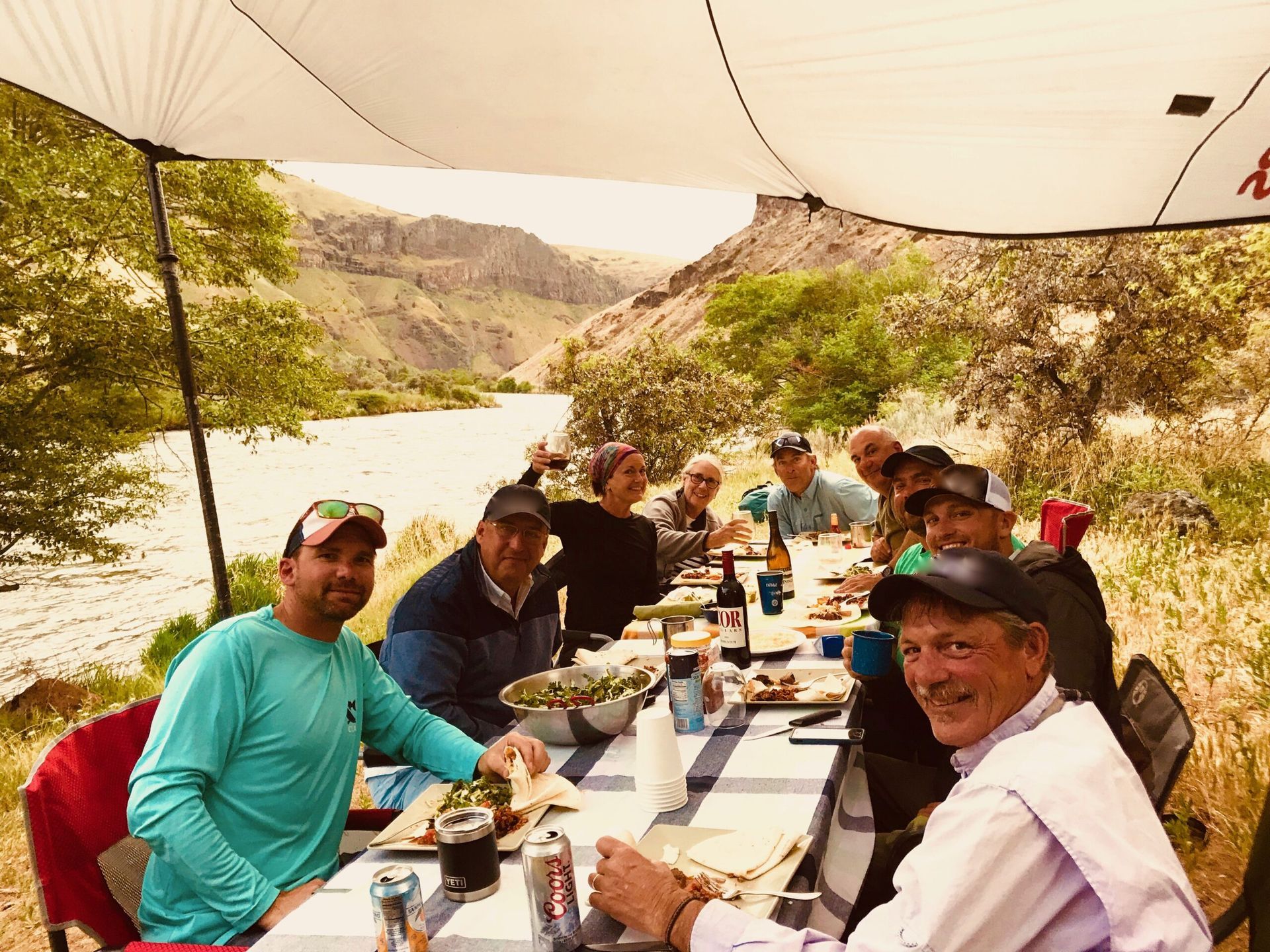 A group of men are sitting at a long table in front of a river.