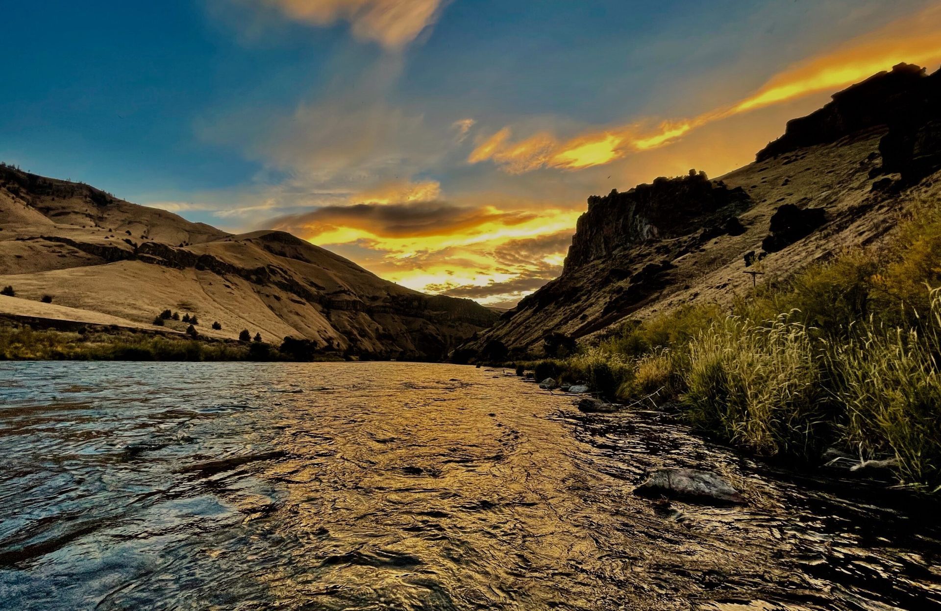 A river with mountains in the background and a sunset in the sky