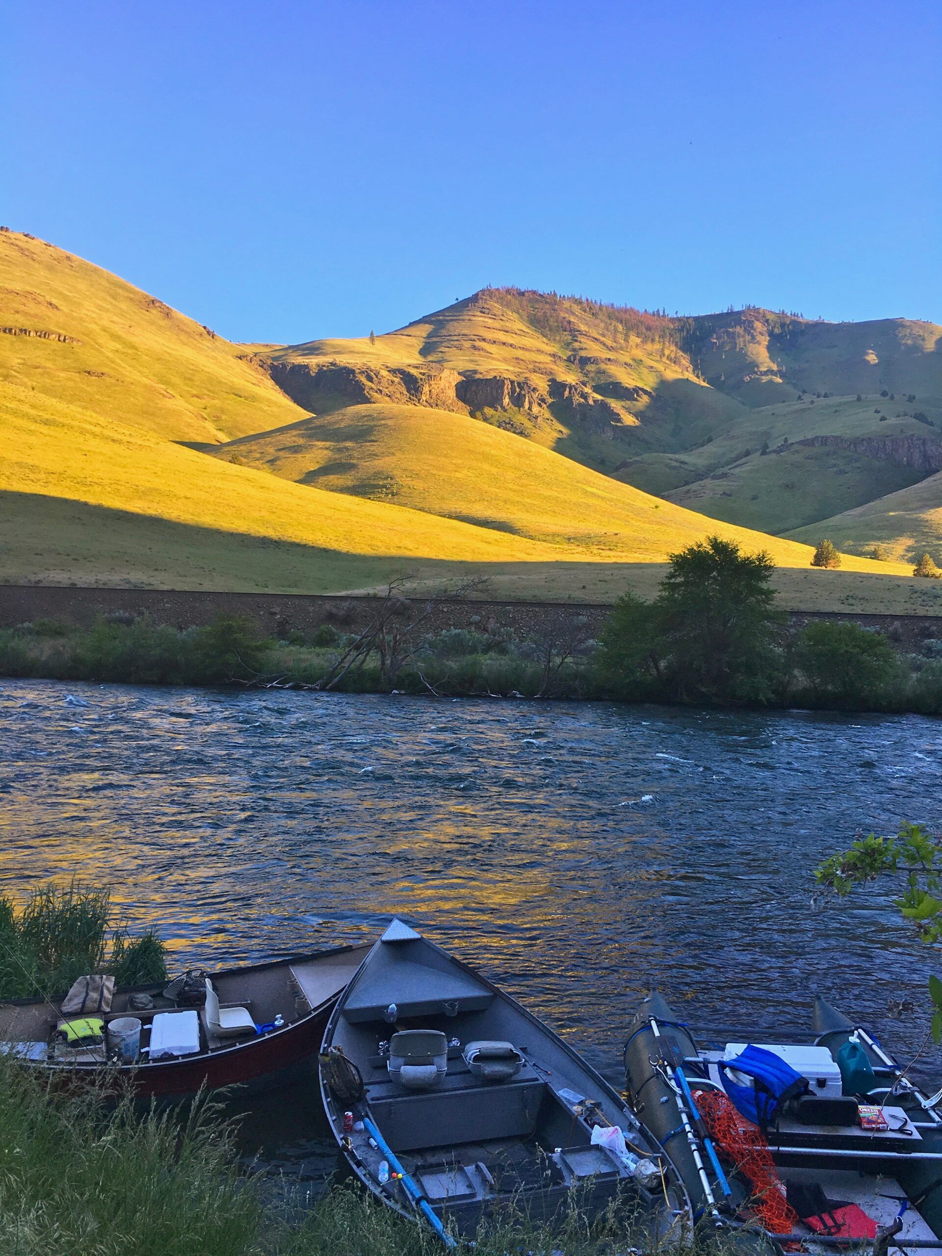 Two boats are sitting on the shore of a river with mountains in the background.