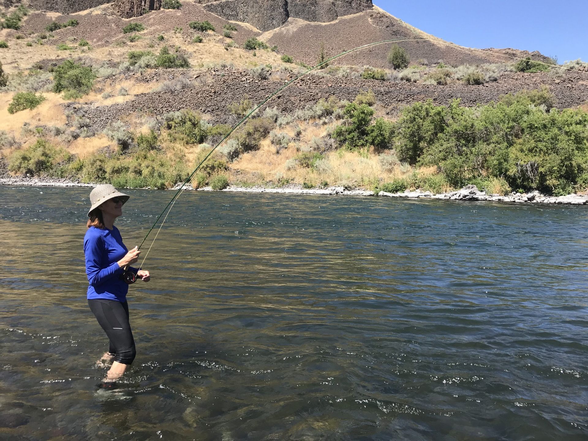A woman is fishing in a river with a fishing rod.