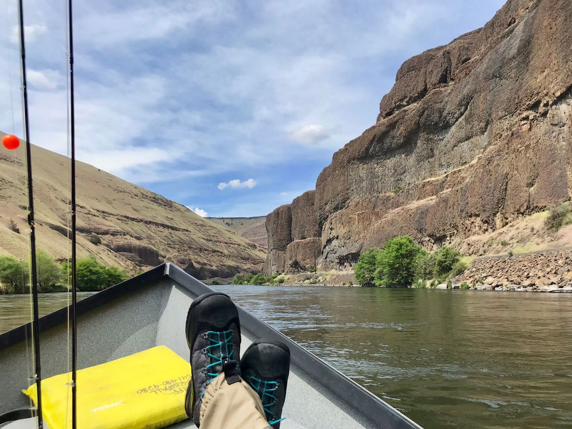A person is sitting in a boat on a river with their feet up.