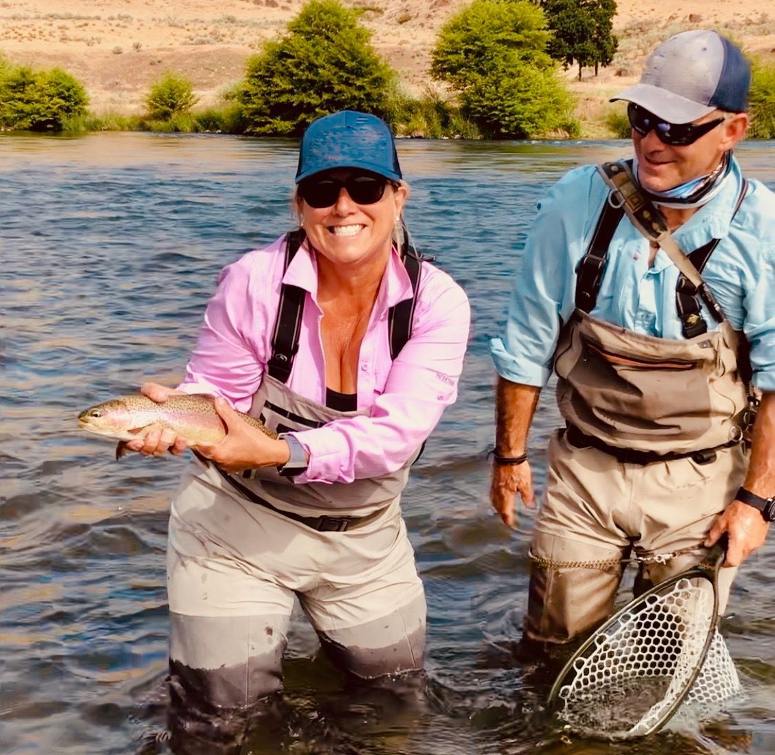 A man and a woman are standing in the water holding a fish.