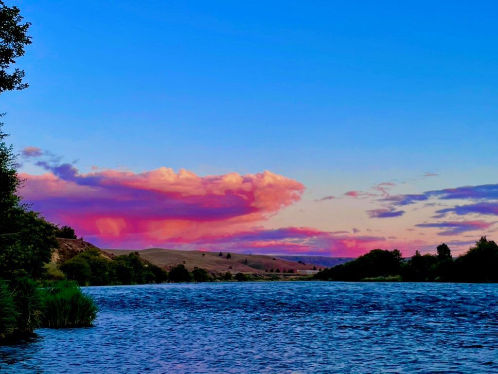 A lake with a sunset in the background and pink clouds in the sky.