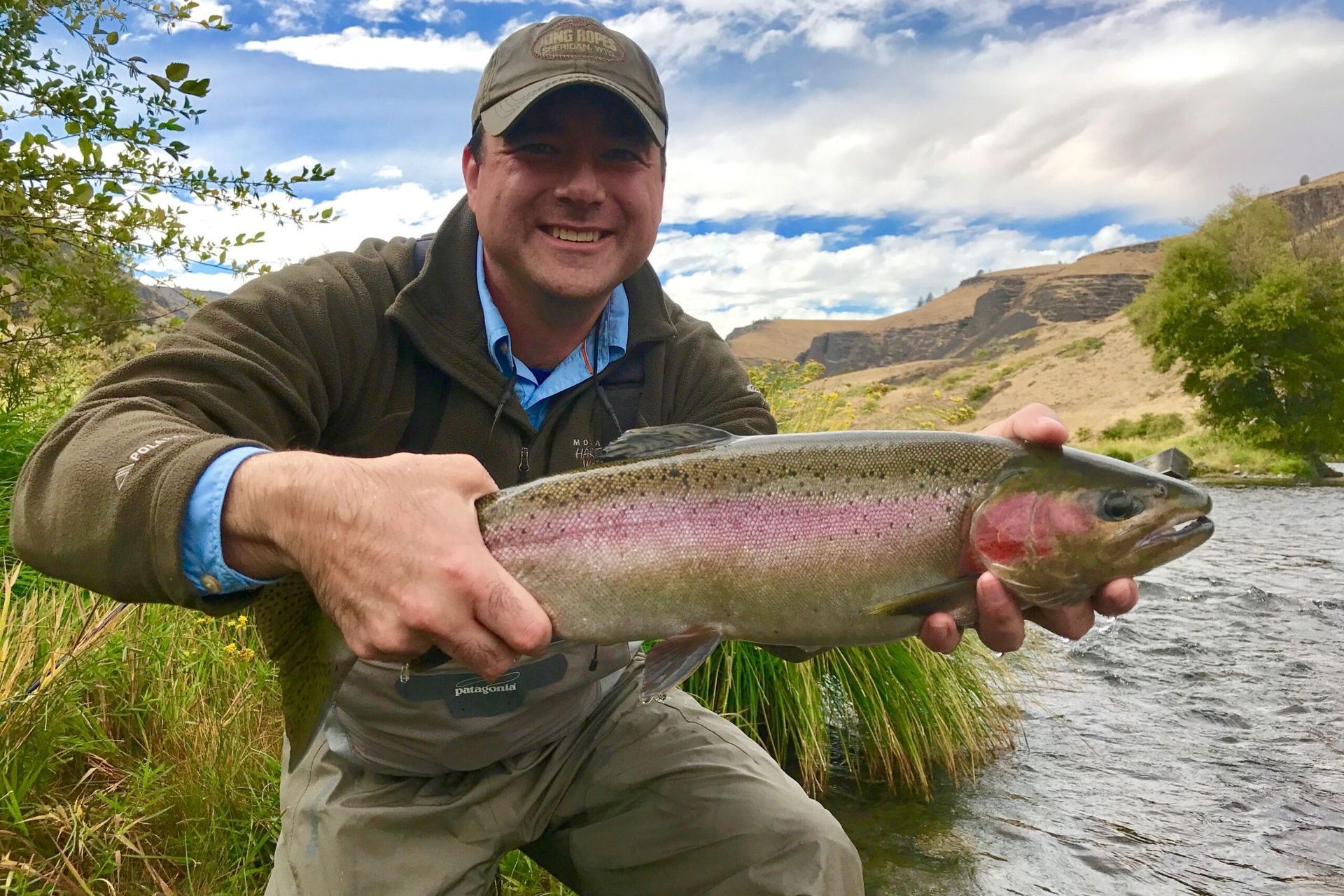 A man is holding a large rainbow trout in his hands.