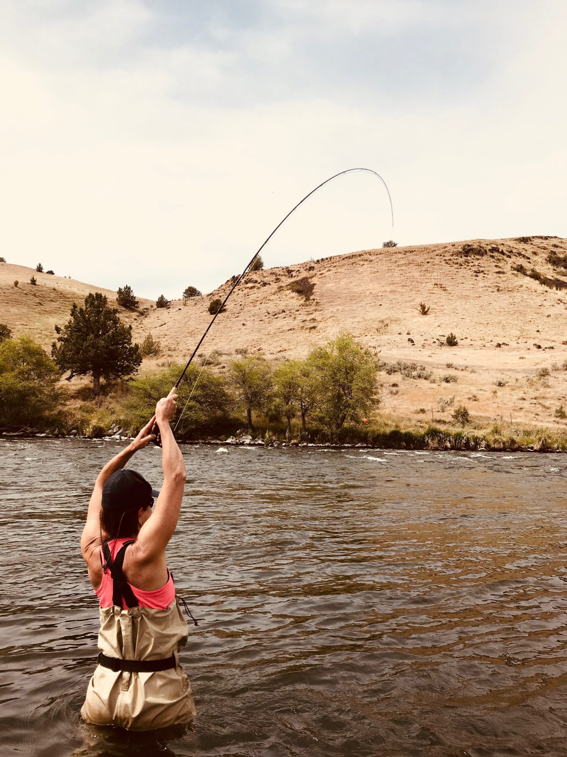 A woman is fishing in a river with a fishing rod.