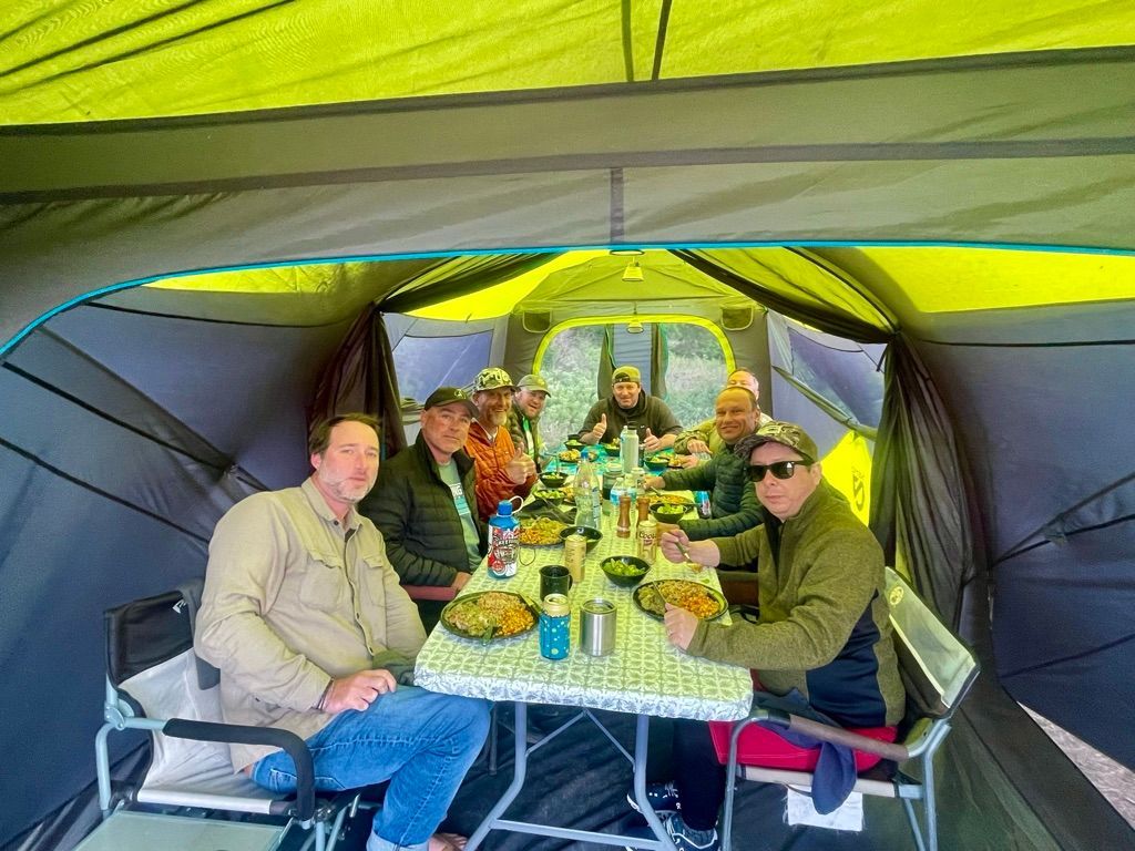 A group of men are sitting at a table in a tent eating food.