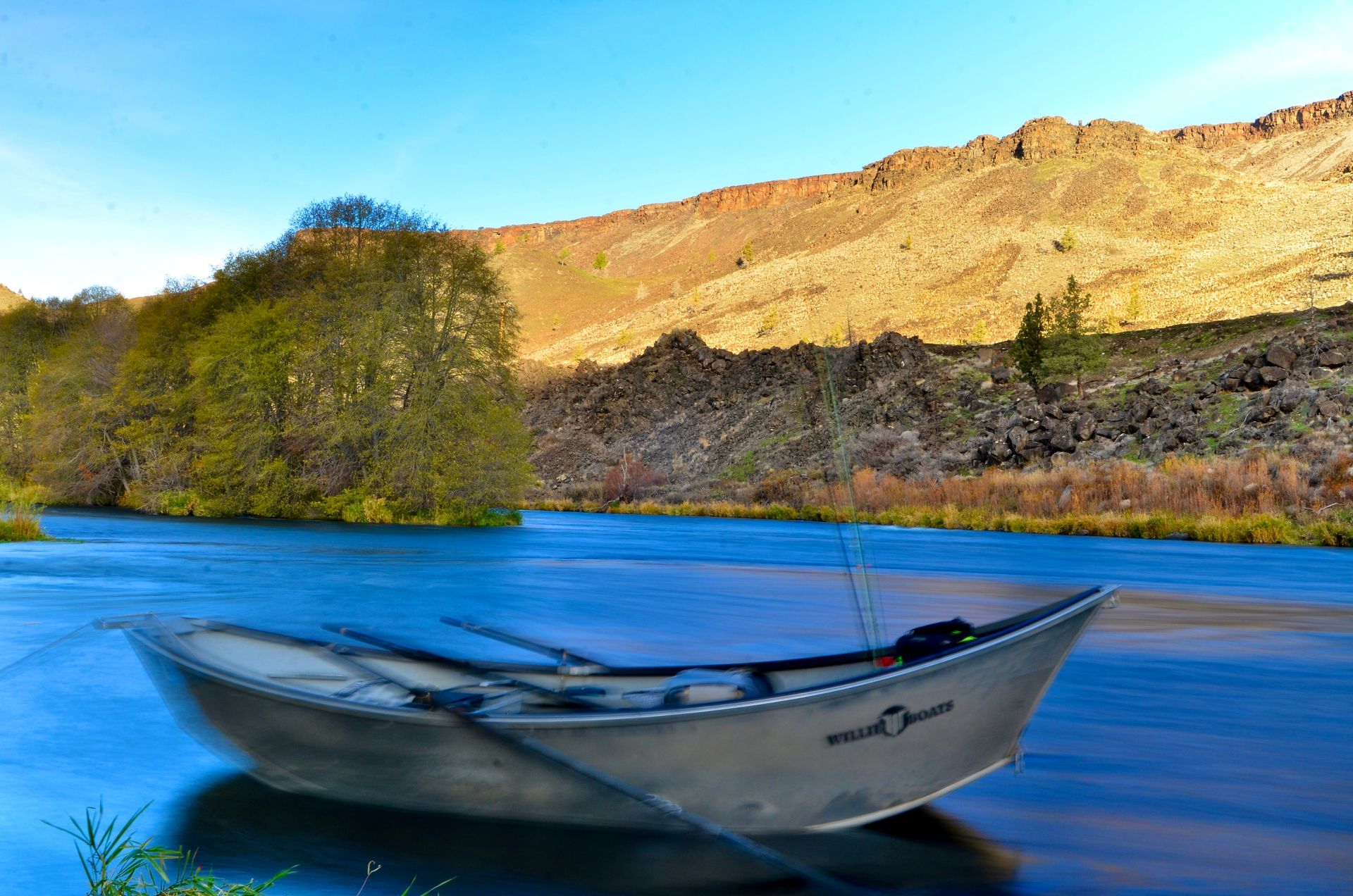 A boat is sitting on the shore of a river with mountains in the background.