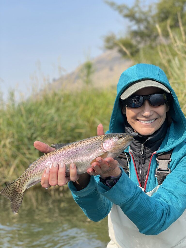 A woman is holding a rainbow trout in her hands.