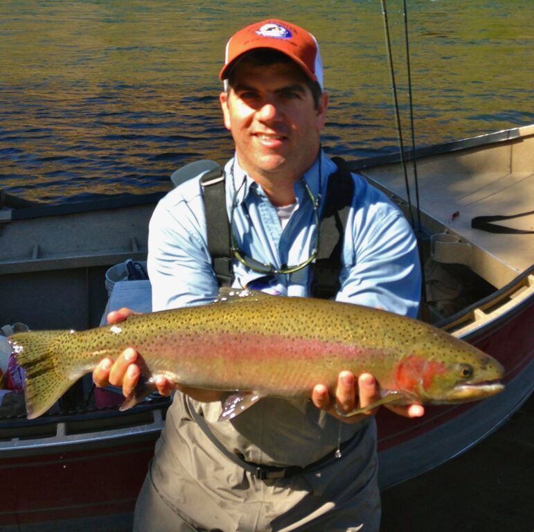 A man holding a rainbow trout in front of a boat