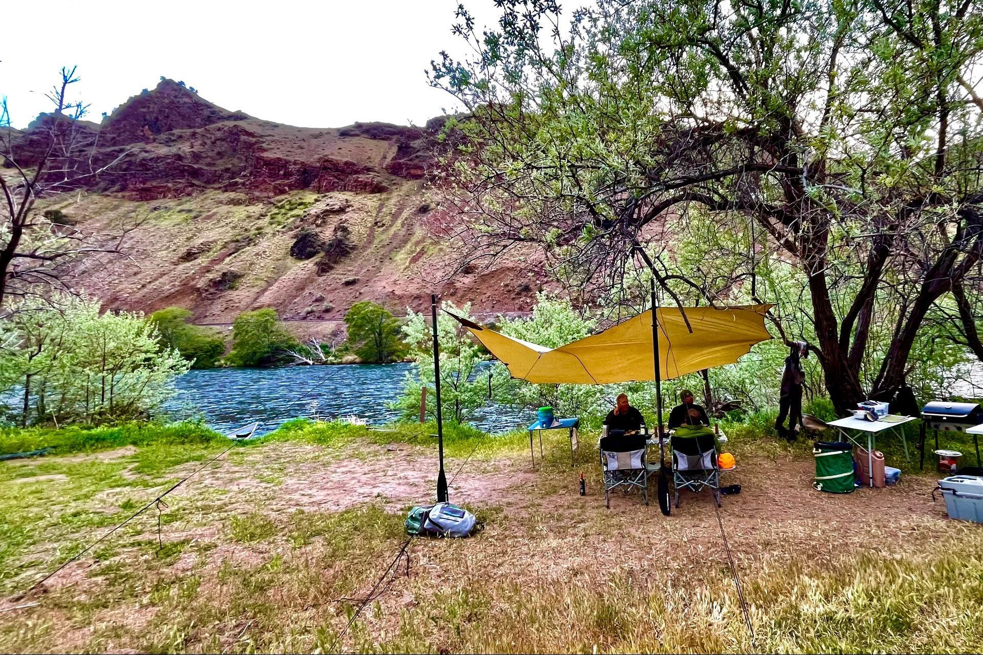 A group of people are sitting under a canopy in a field next to a lake.