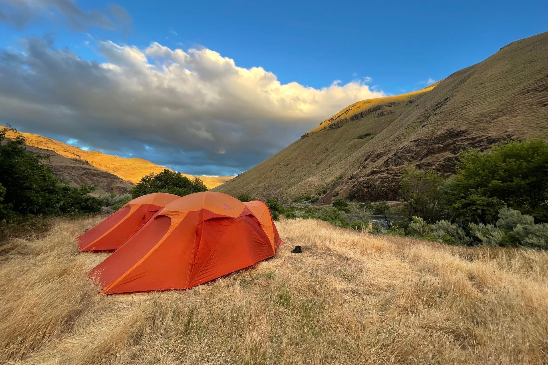 Two orange tents are sitting in a field with mountains in the background.