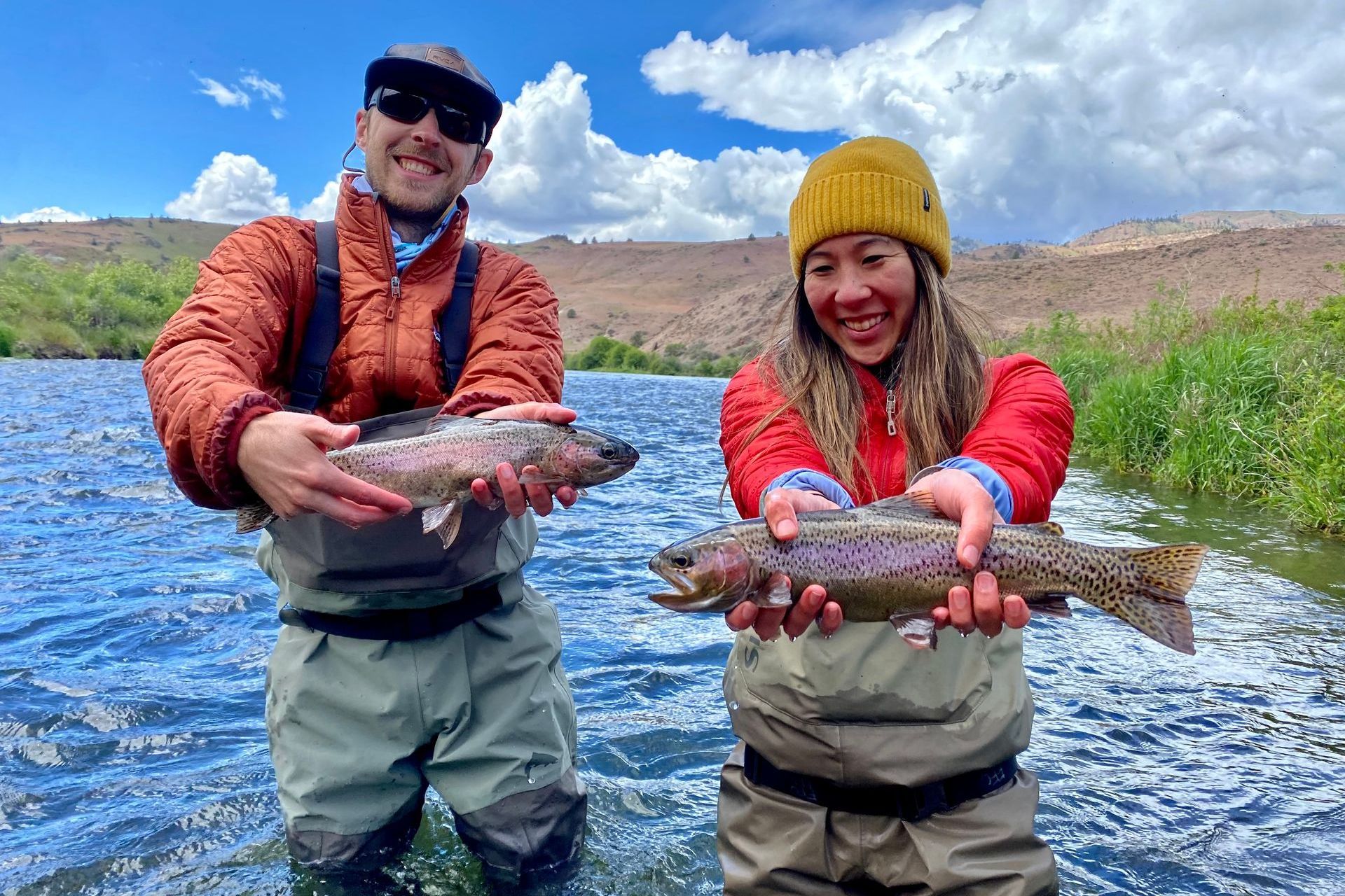 A man and a woman are holding a rainbow trout in a river.