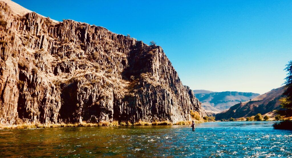 A river with a cliff in the background and mountains in the background.