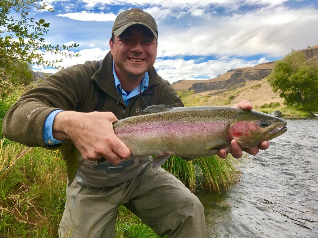 A man is holding a large rainbow trout in his hands.