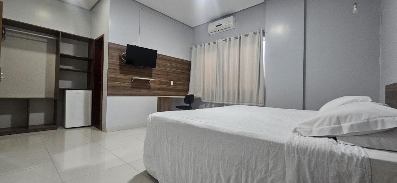 Um quarto de hotel com cama, televisão, escrivaninha e geladeira.