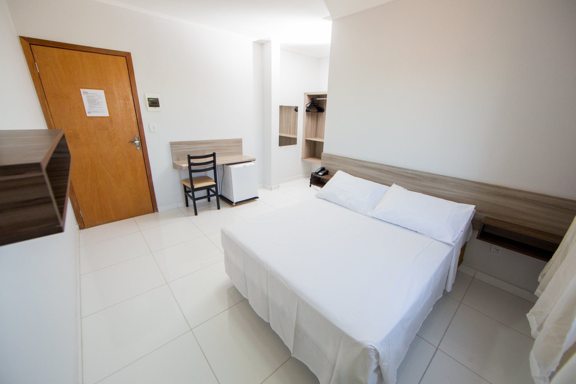 Um quarto de hotel com uma cama, cadeira, escrivaninha e porta.