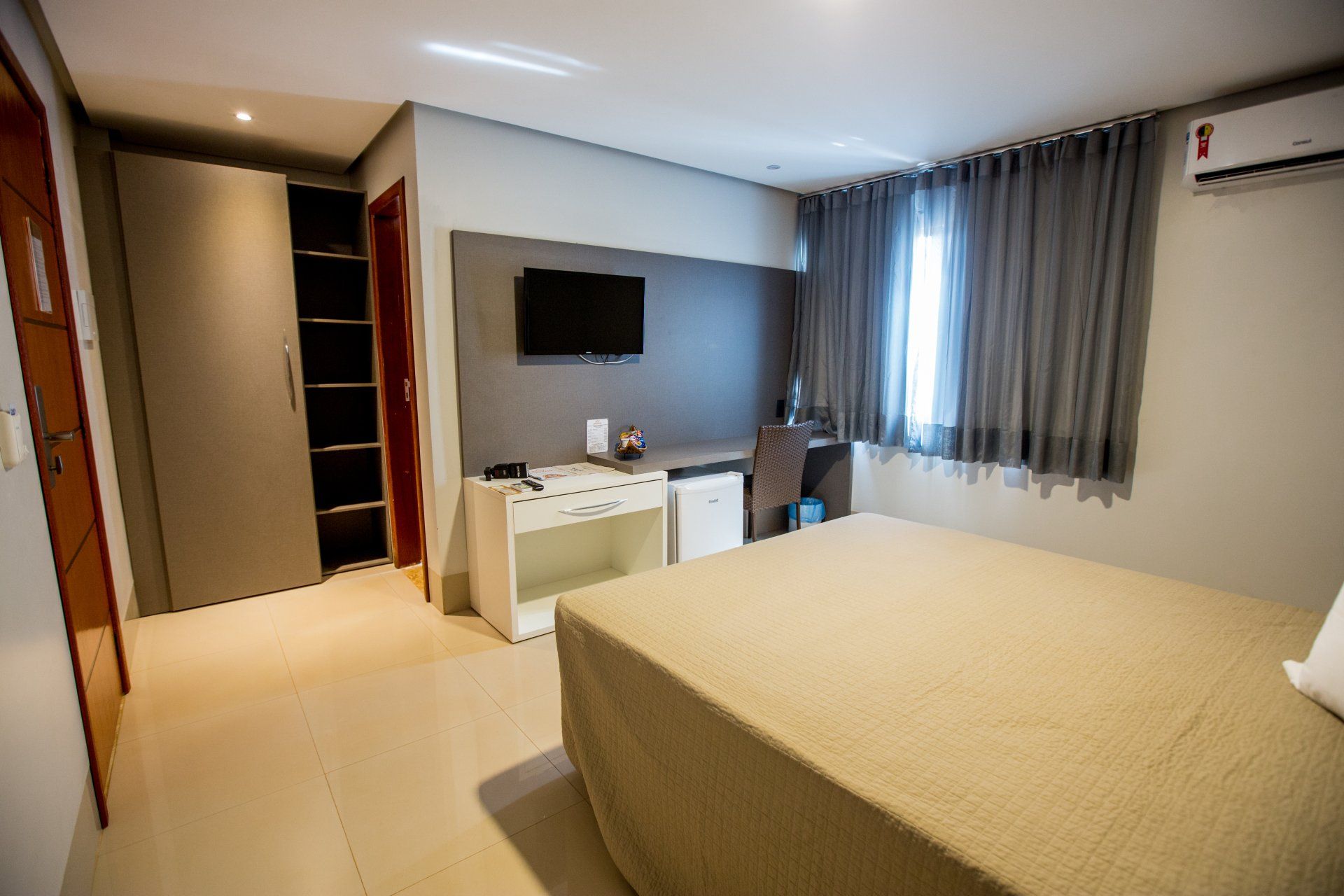 Um quarto de hotel com cama, escrivaninha, televisão e armário.