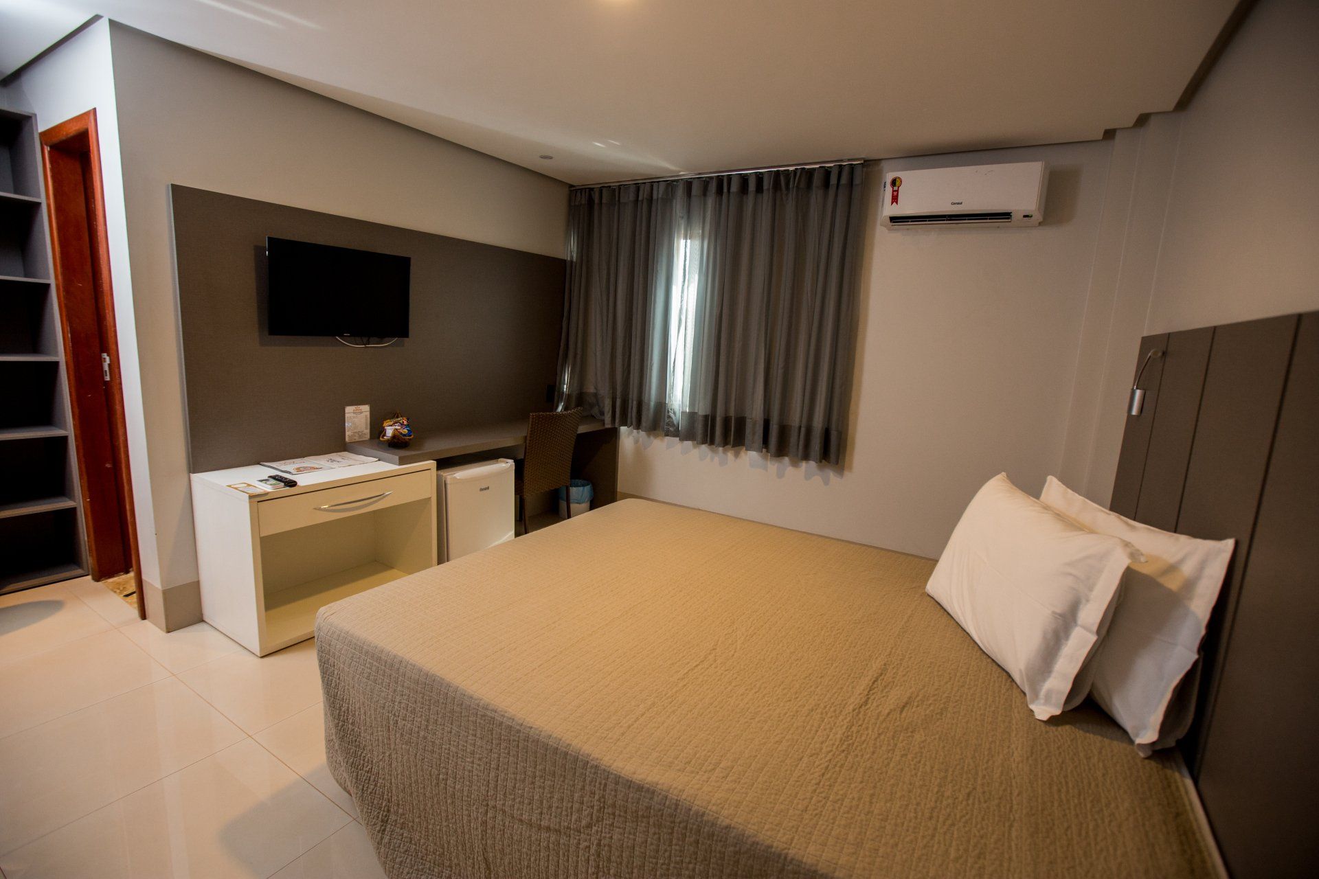 Um quarto de hotel com cama, escrivaninha, televisão e ar condicionado.