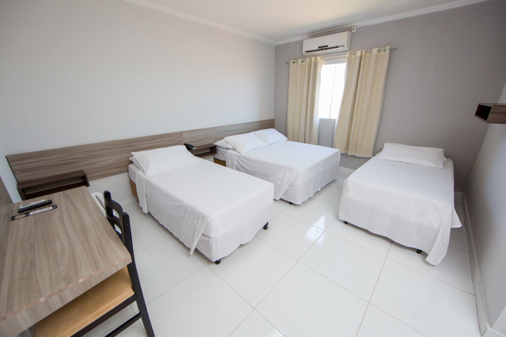 Um quarto de hotel com três camas e uma escrivaninha.