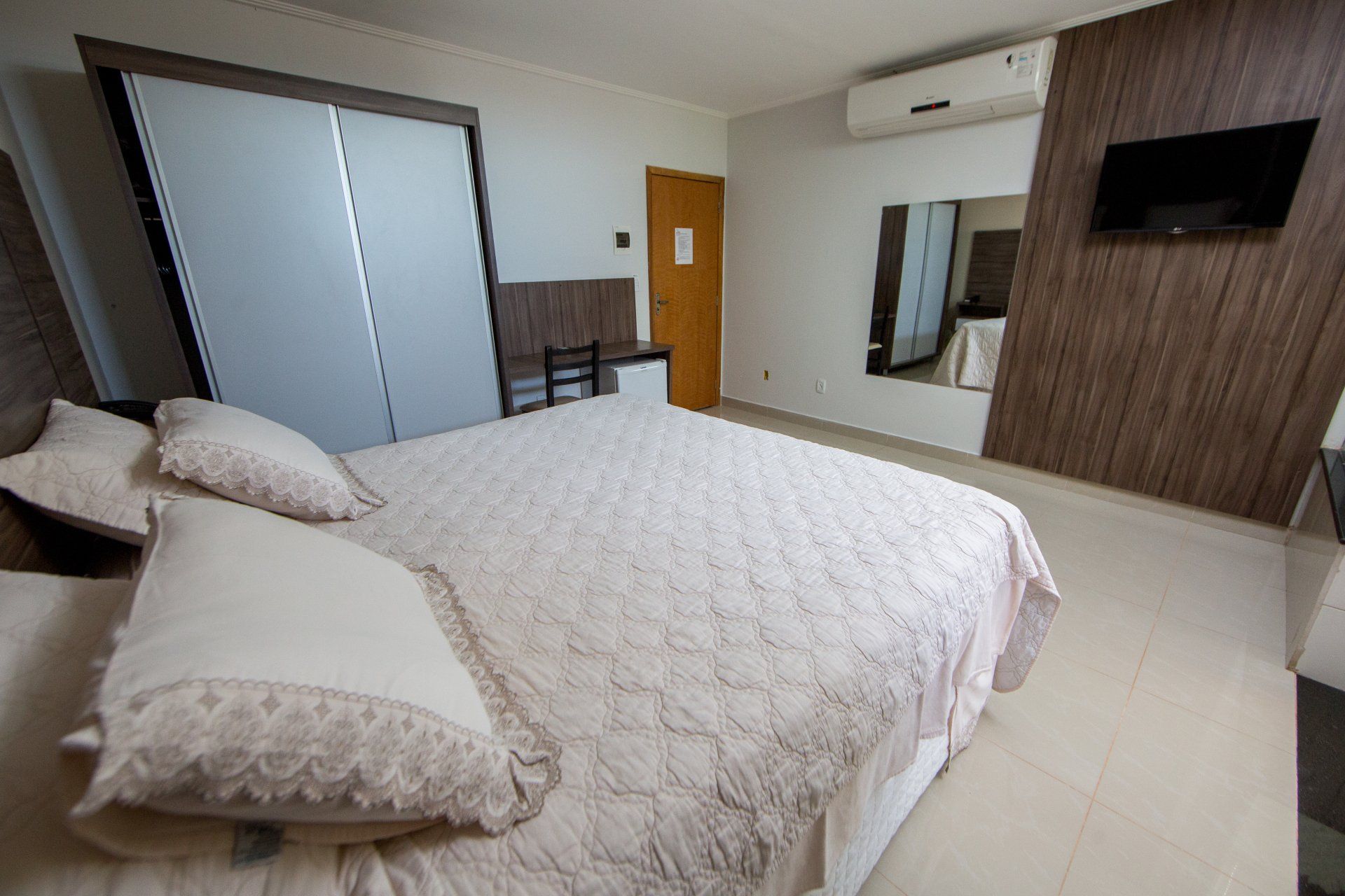 Um quarto com uma cama grande, uma televisão, um armário e um espelho.