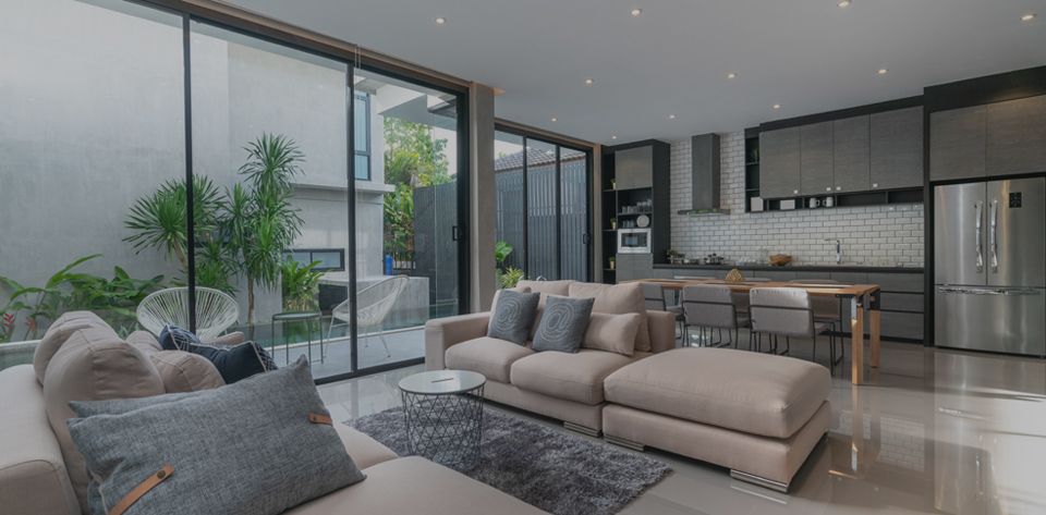 Modern living room and kitchen. Neutral colors, large windows, sectional sofa, stainless steel appliances.