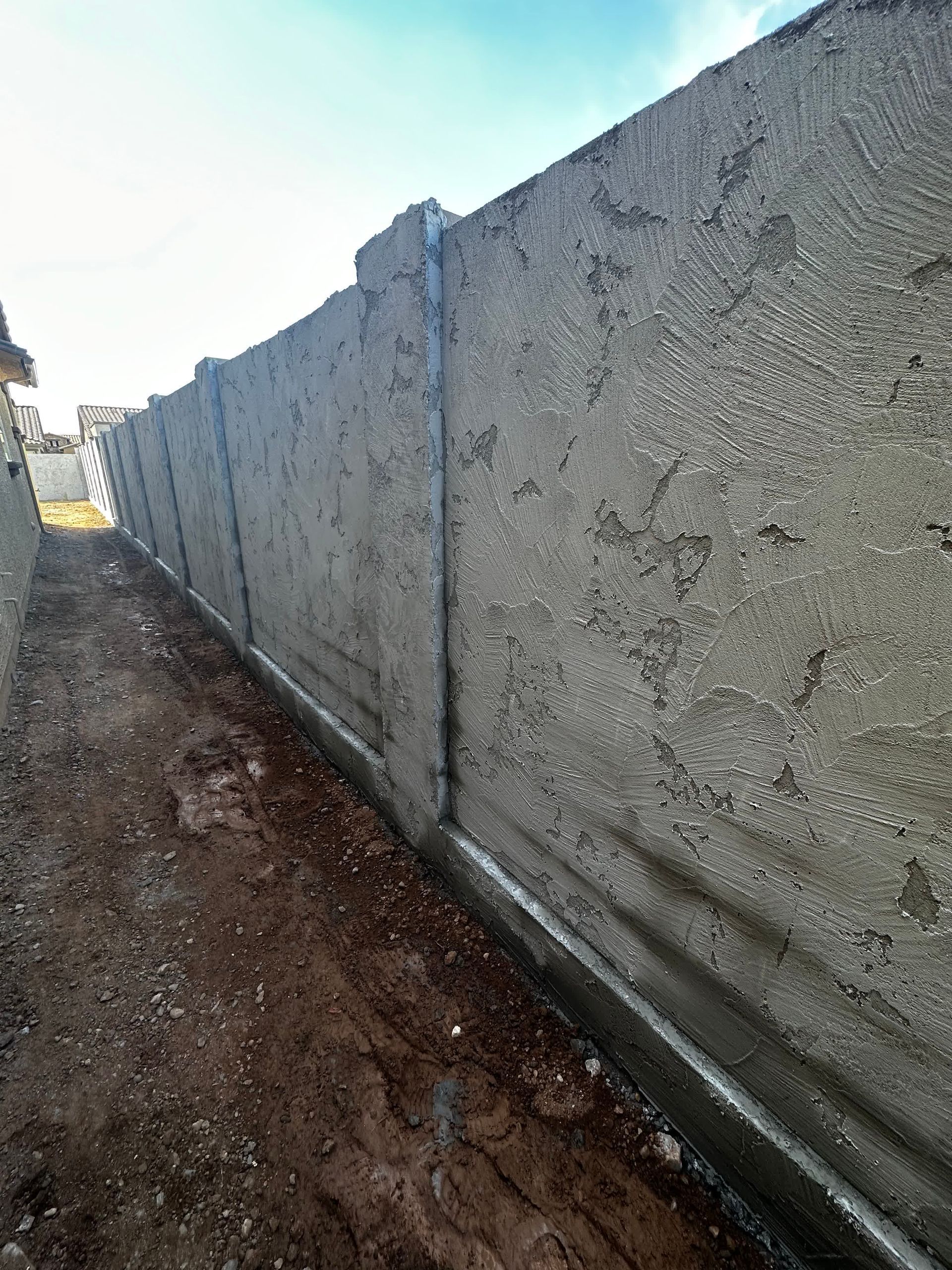 A concrete fence is being built next to a dirt path.