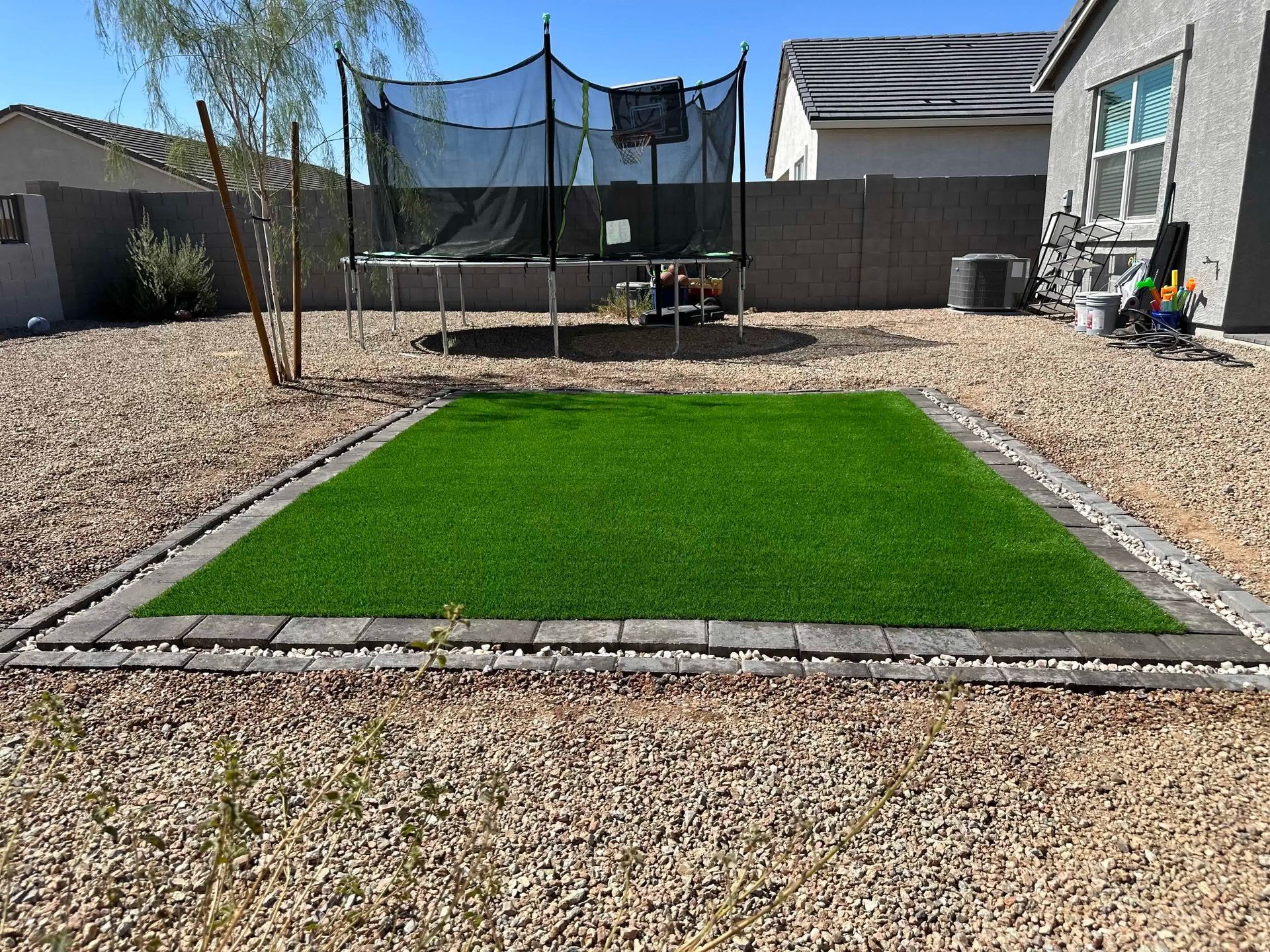 A backyard with a trampoline and a lawn in the middle of it.