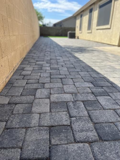 A brick walkway leading to a house with a brick wall in the background.