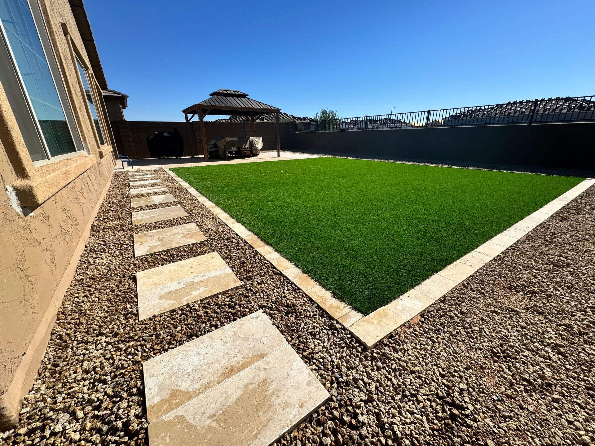 A lawn with a walkway leading to it and a gazebo in the background.