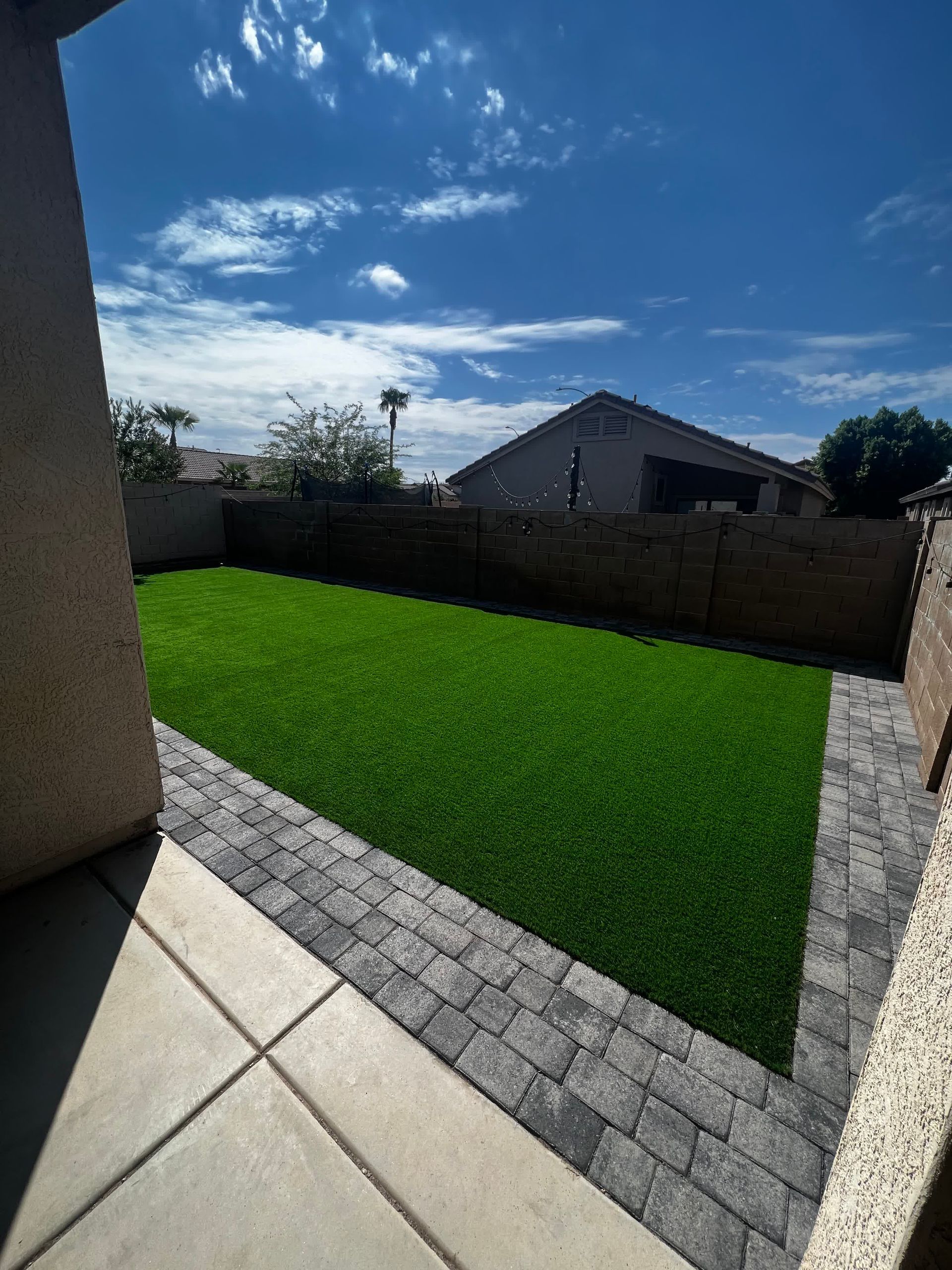 A backyard with a lush green lawn and a brick walkway.