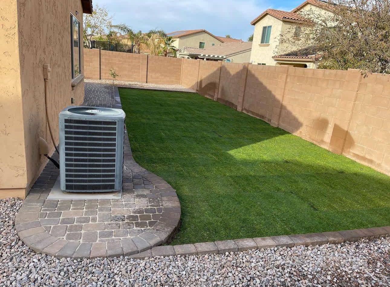 A backyard with a lawn and a patio with a air conditioner.