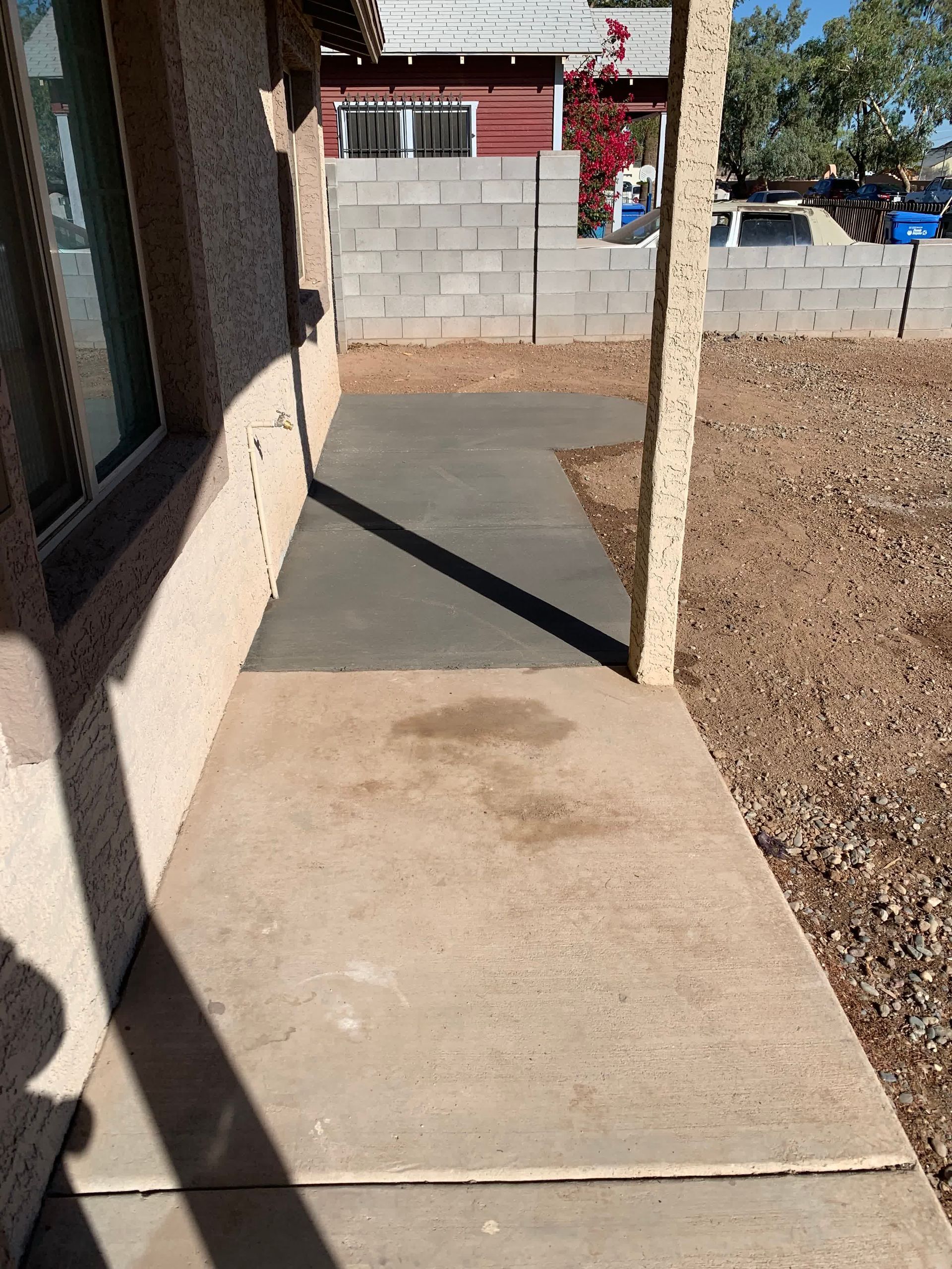 A concrete walkway leading to a house with a brick wall in the background.