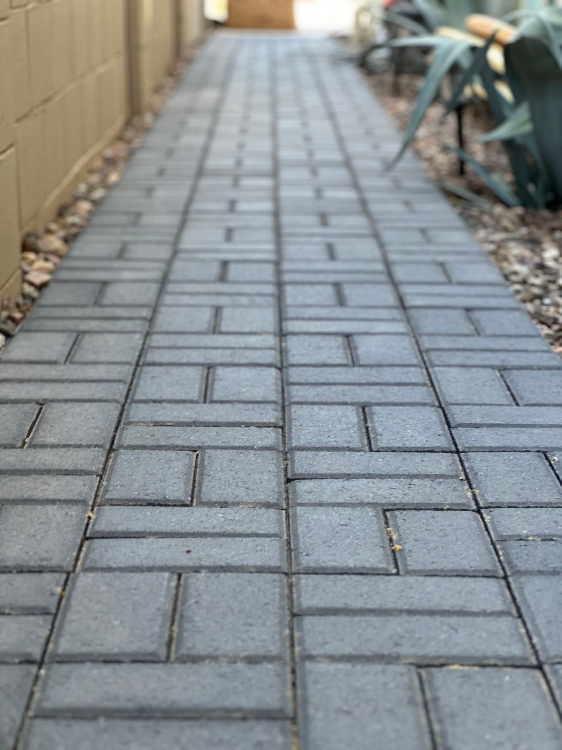 A walkway made of bricks is going down a sidewalk next to a brick wall.