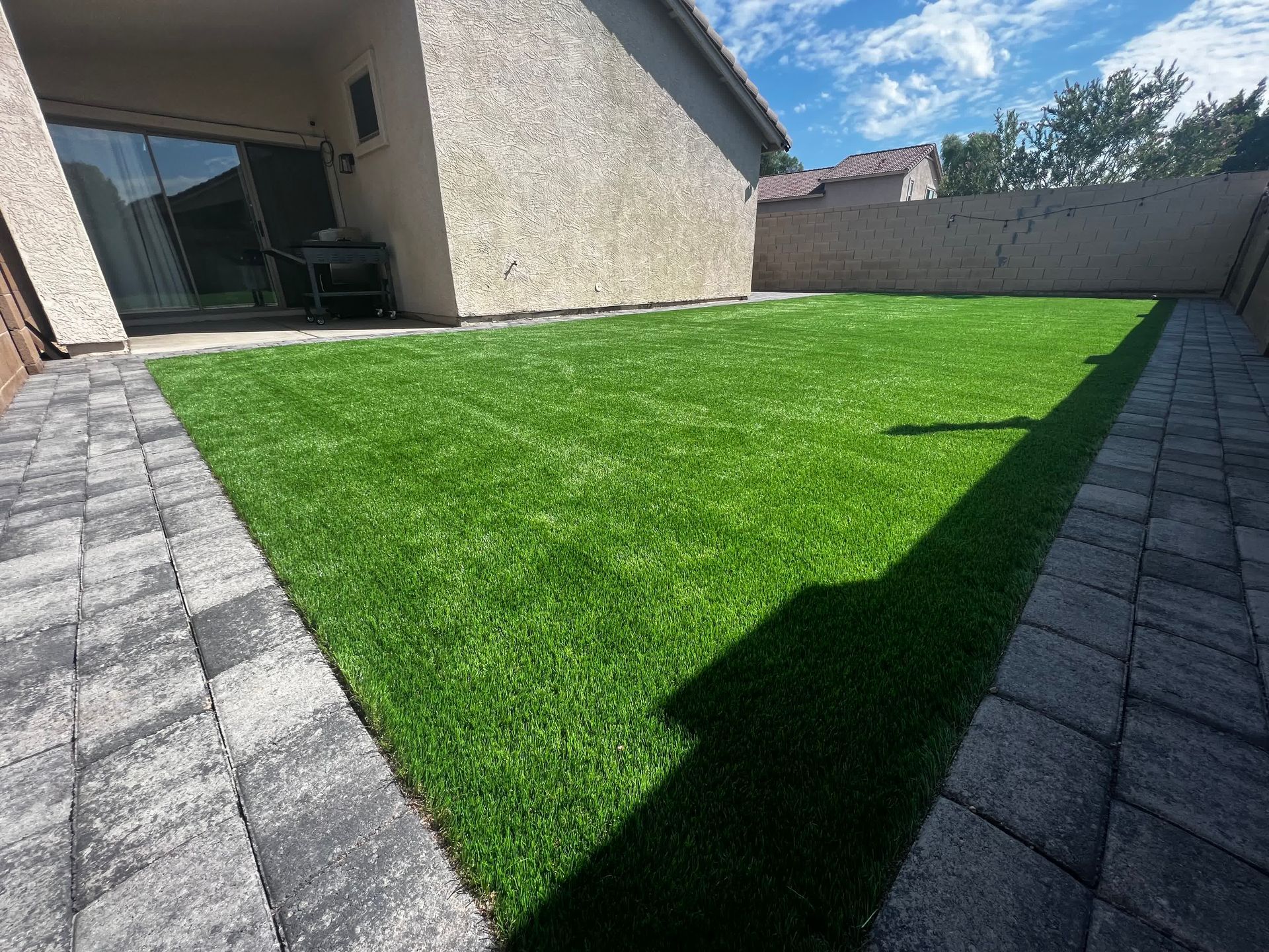 A backyard with a lush green lawn and a brick walkway.
