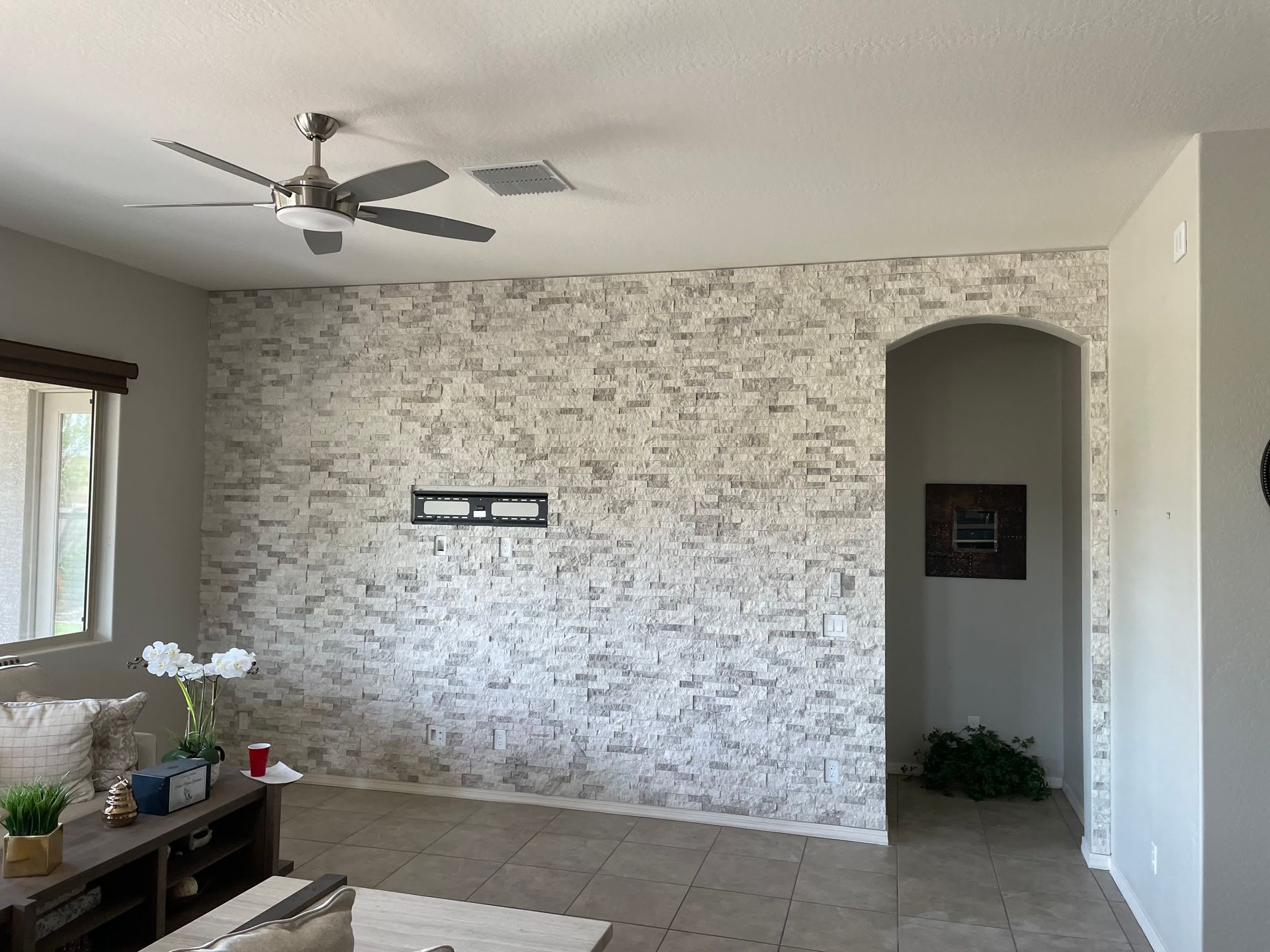 A living room with a ceiling fan and a brick wall.