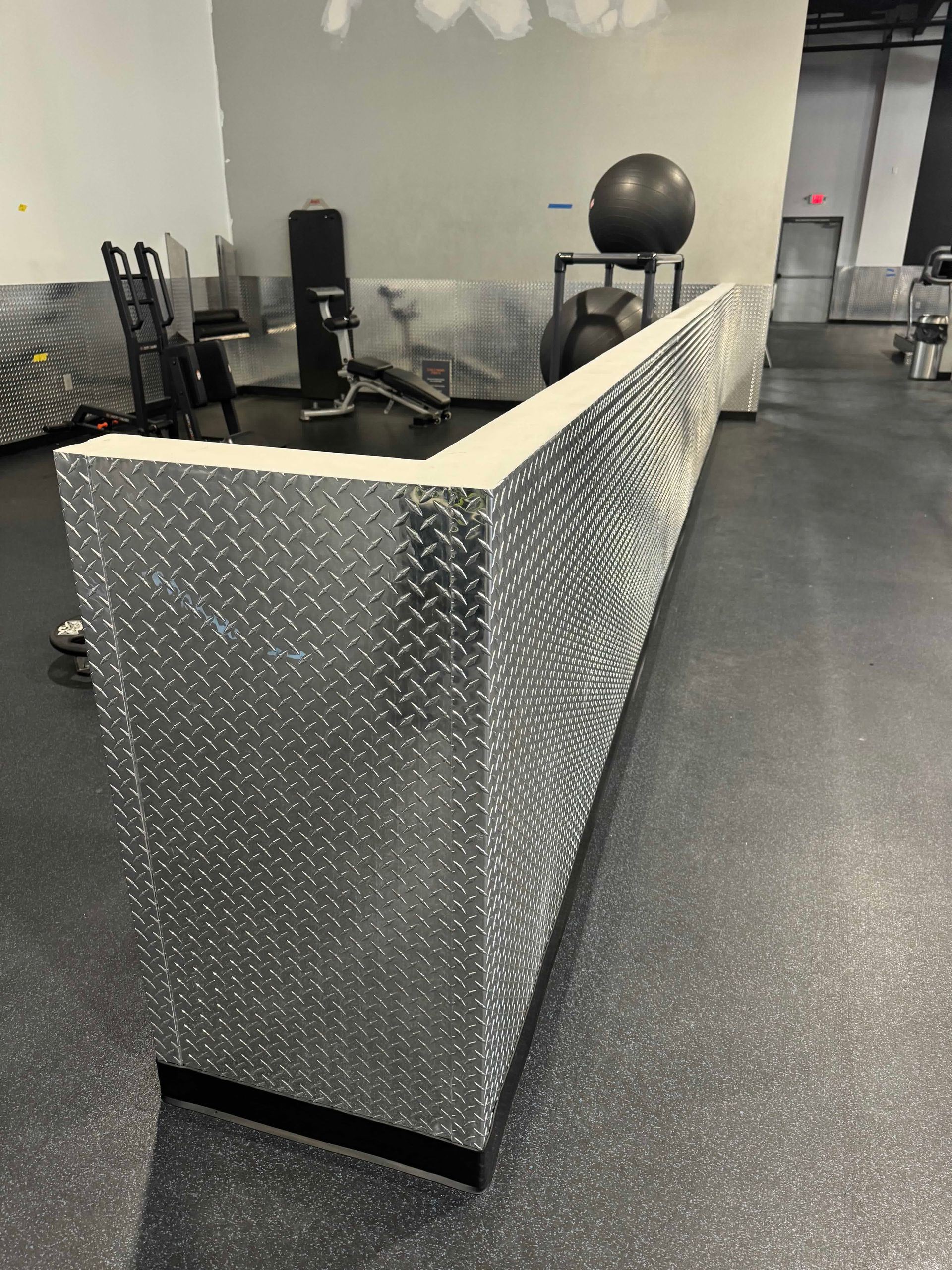A silver couch is sitting in a gym next to a exercise ball.
