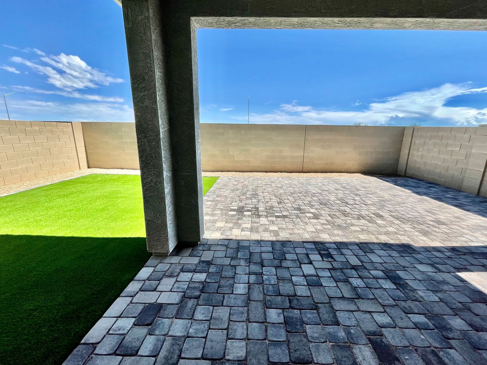 A brick driveway leading to a backyard with a lush green lawn.
