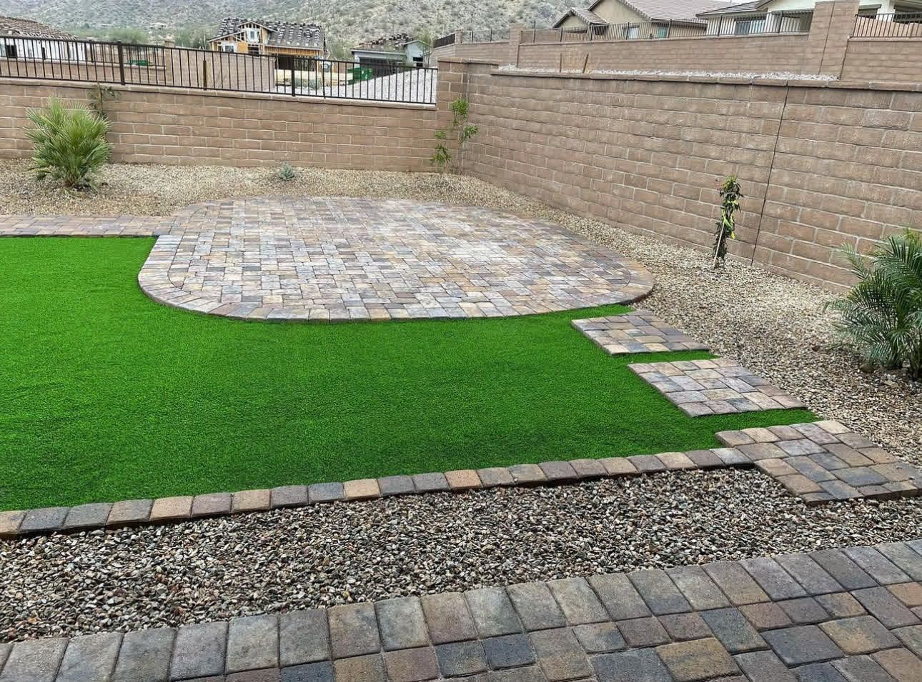 A backyard with a brick walkway and a lush green lawn.