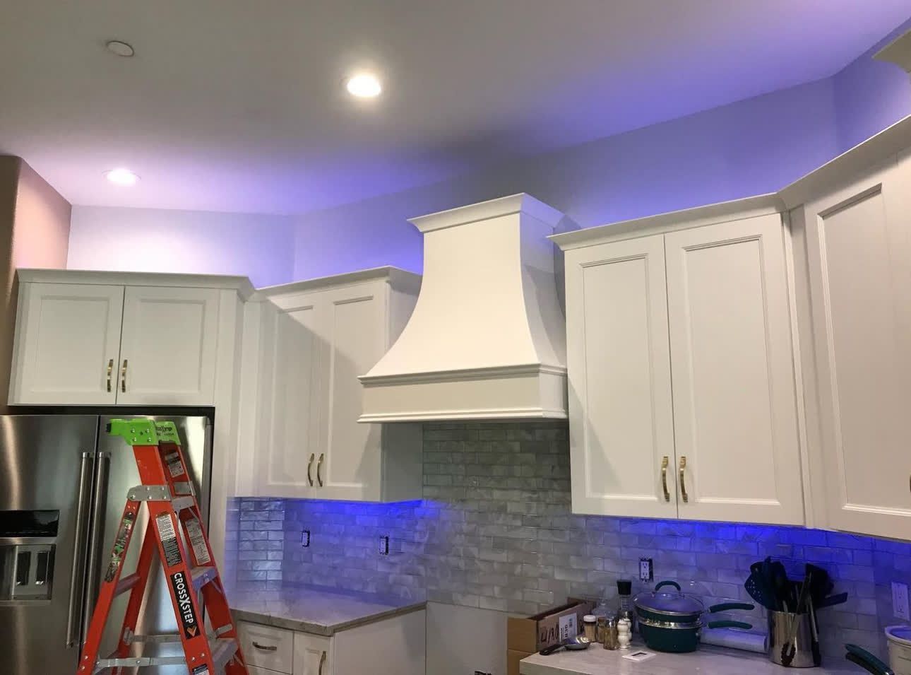 A kitchen with white cabinets and blue lights on the ceiling.
