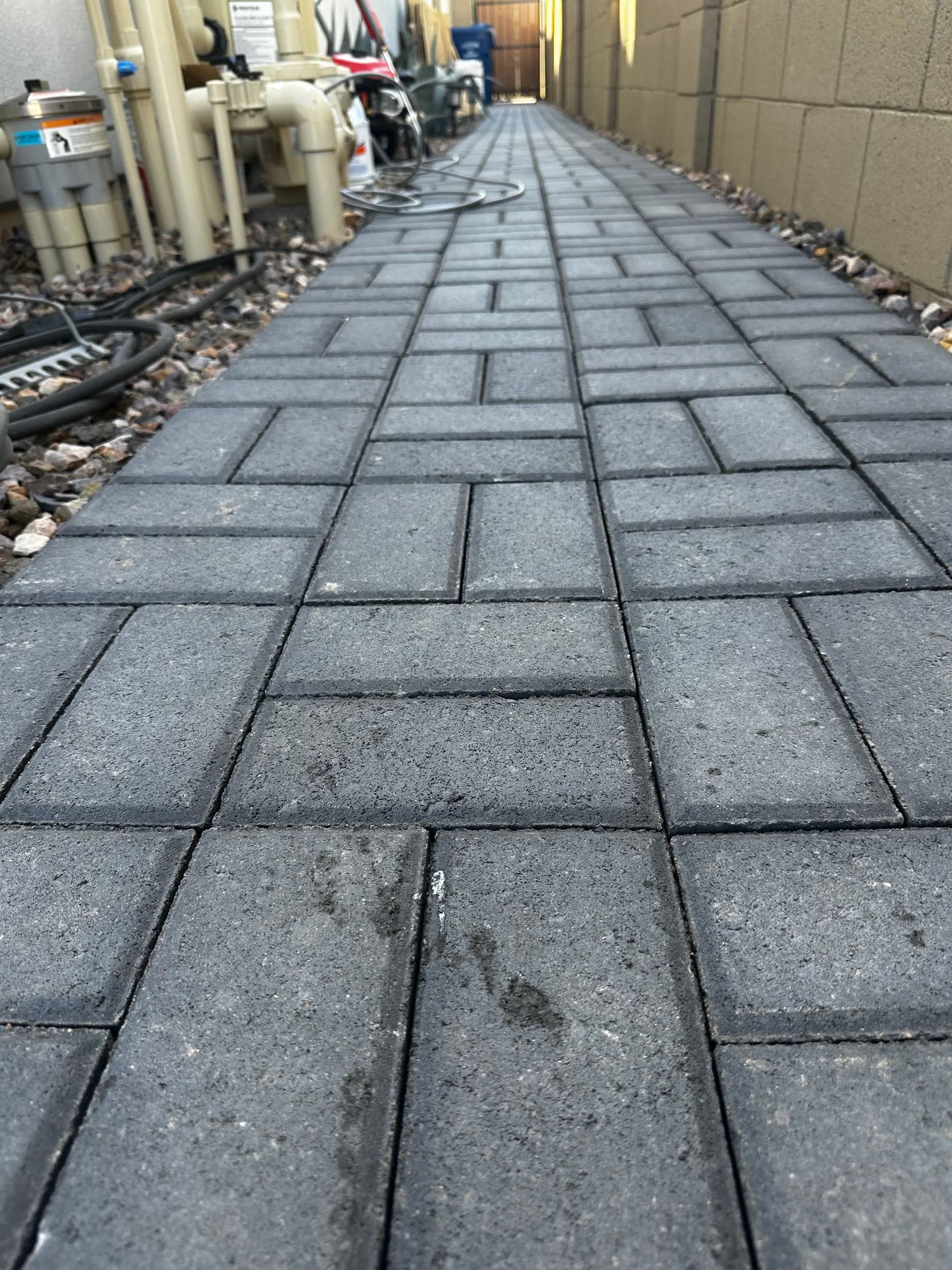 A brick walkway leading to a building with pipes on the side.