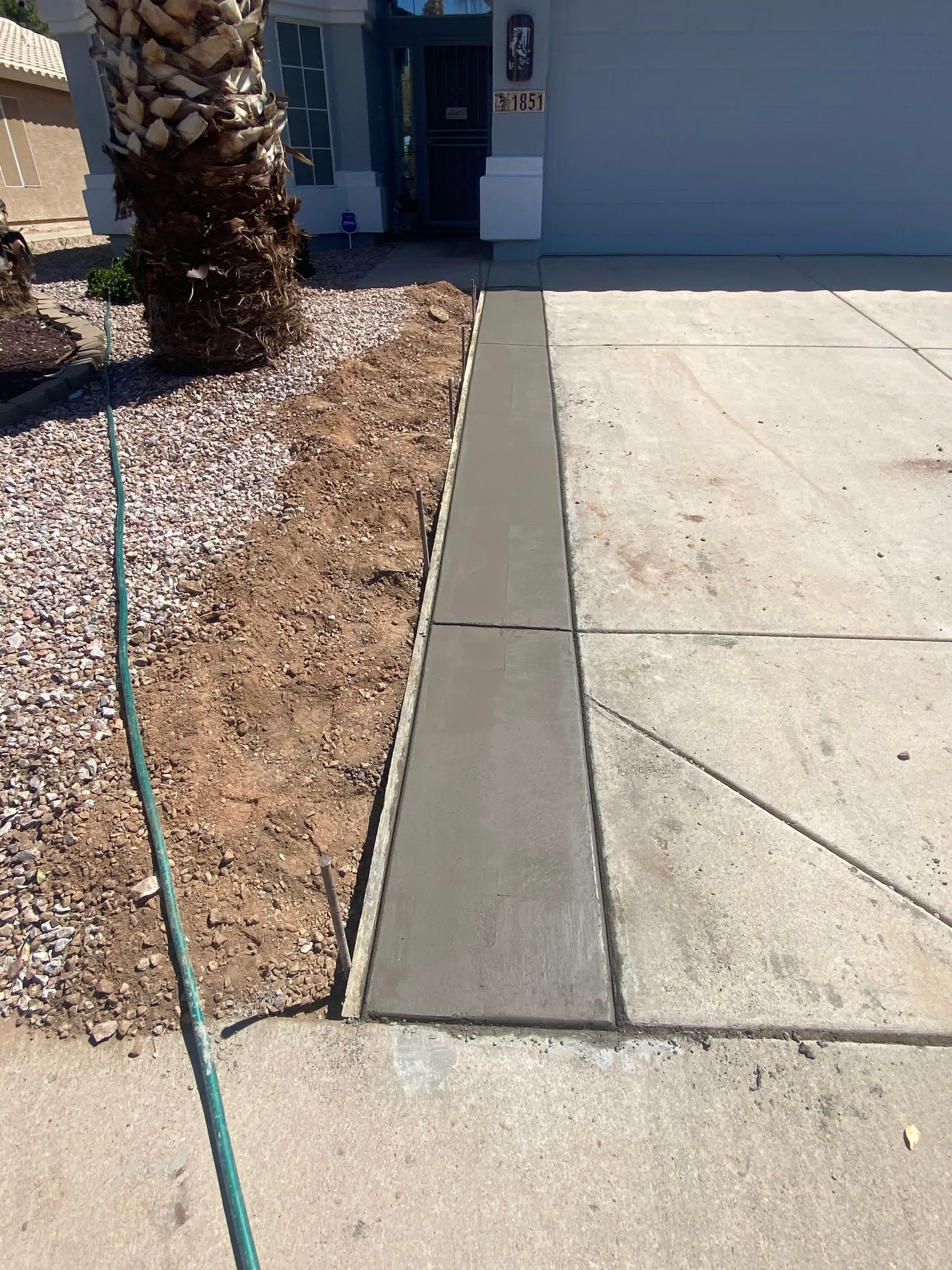 A hose is laying on the sidewalk in front of a house.