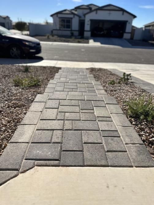 A brick walkway leading to a house with a car parked on the side of the road.