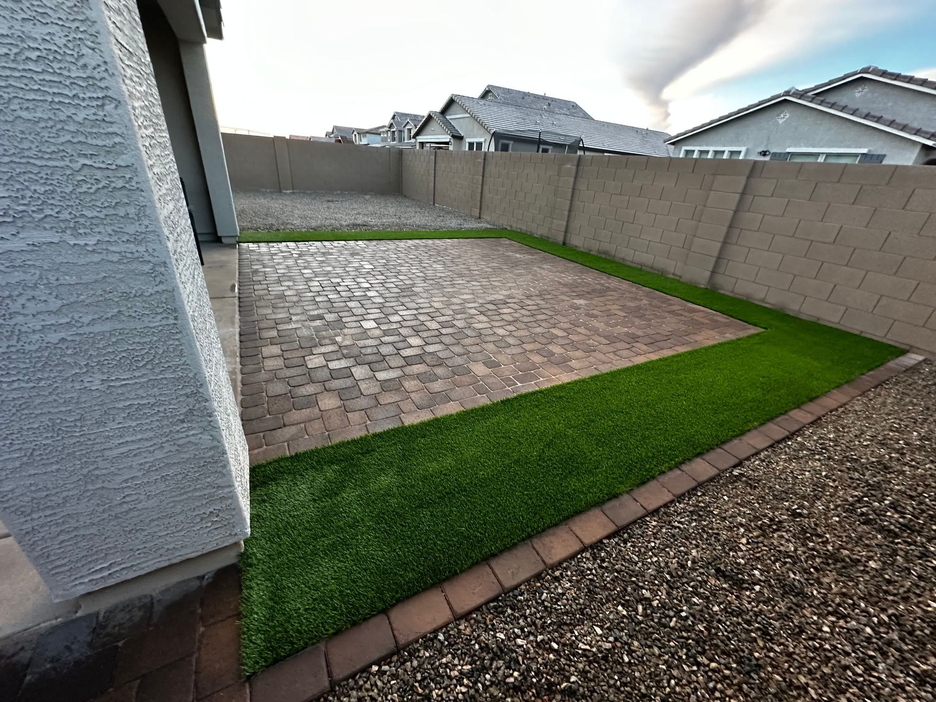 A backyard with a brick walkway and artificial grass.
