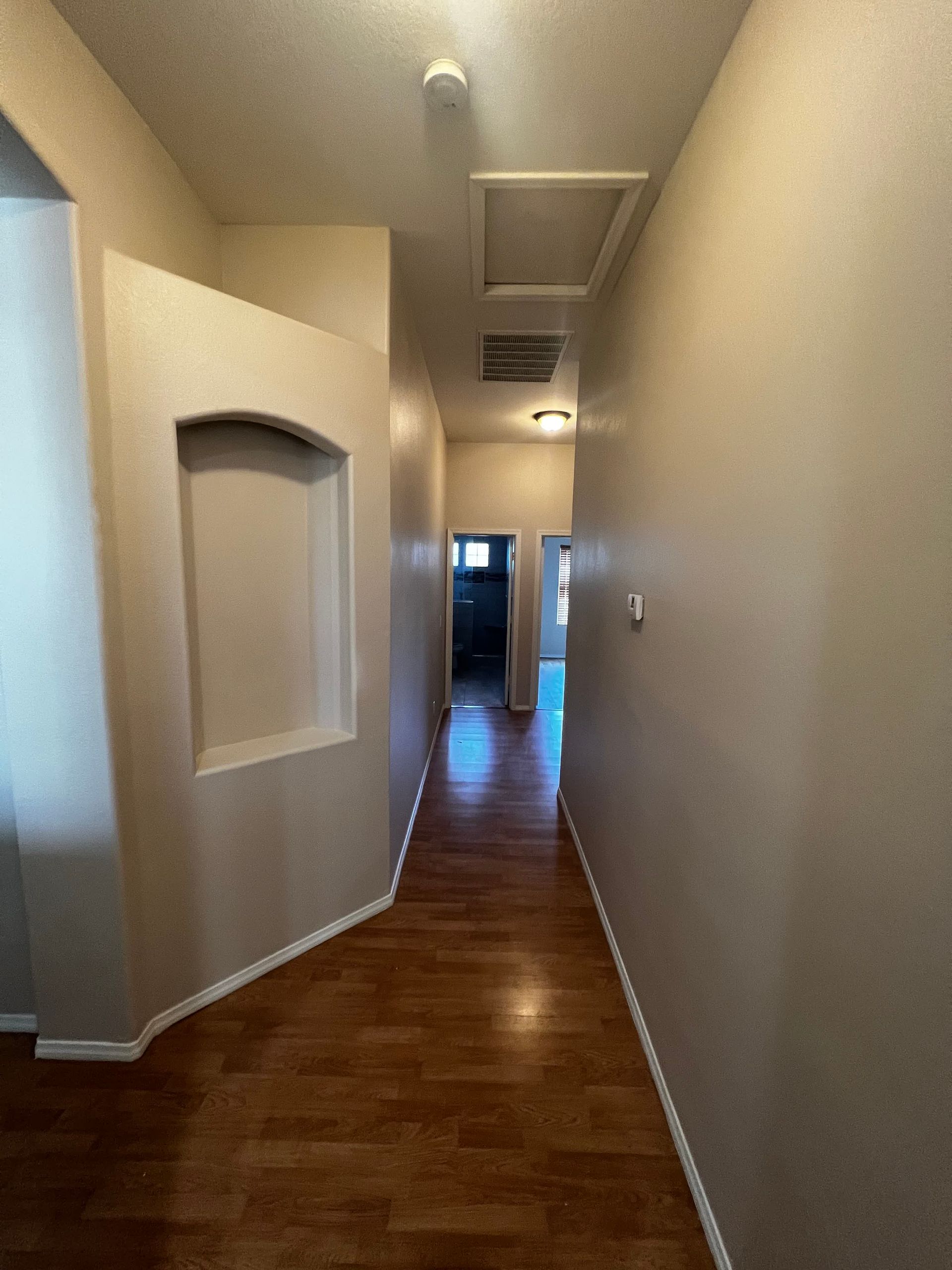 A long hallway with hardwood floors and gray walls in a house.