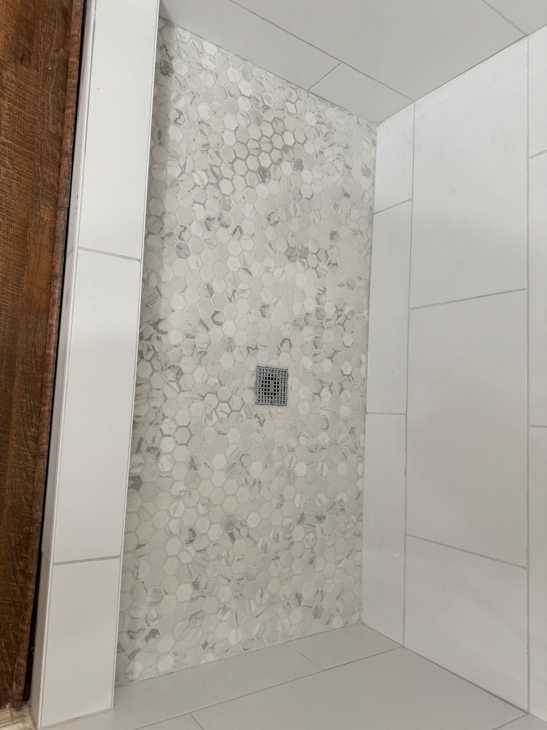 A shower stall with white tiles on the wall and floor.