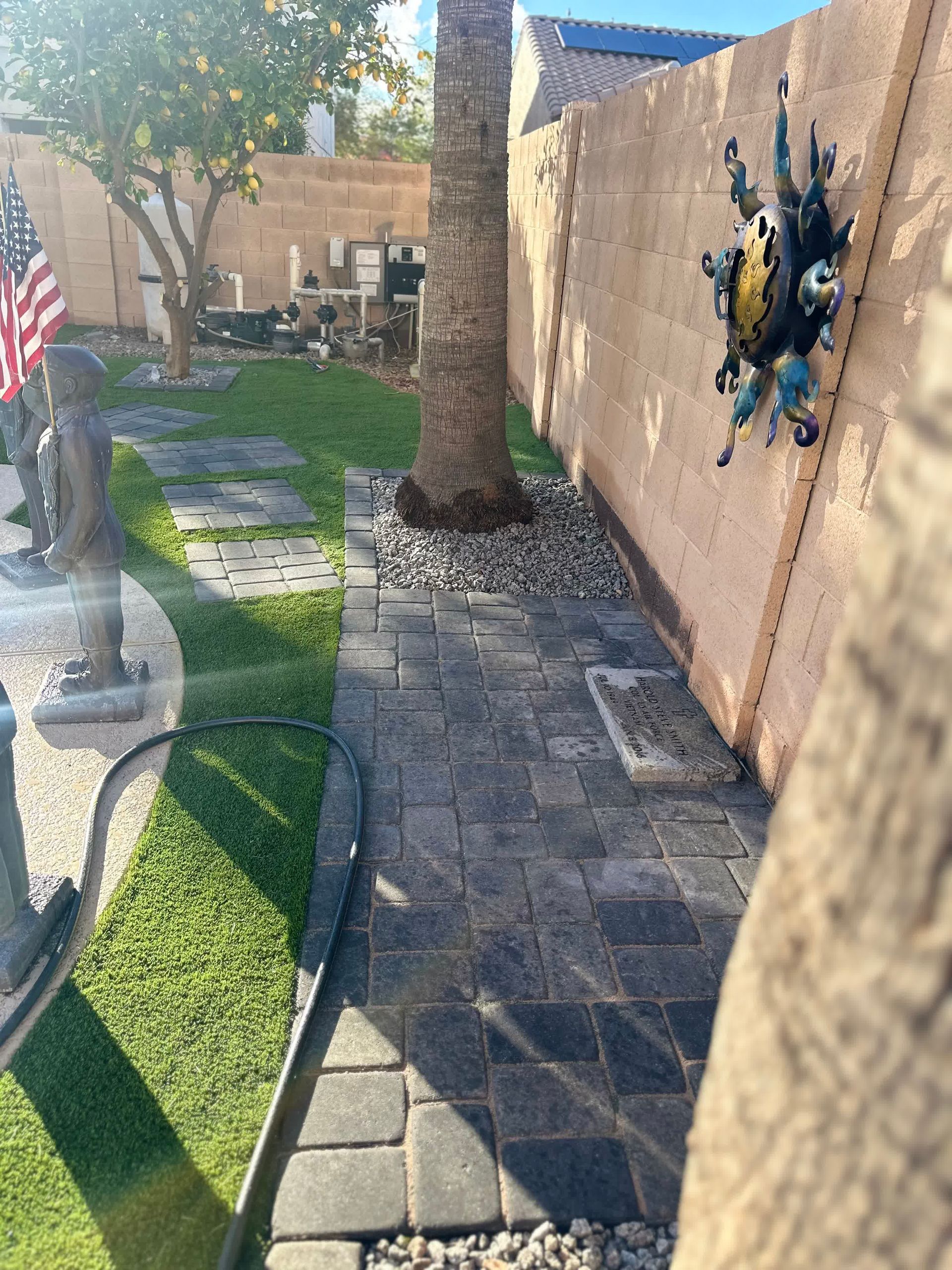 A brick walkway leading to a backyard with a palm tree and an american flag.