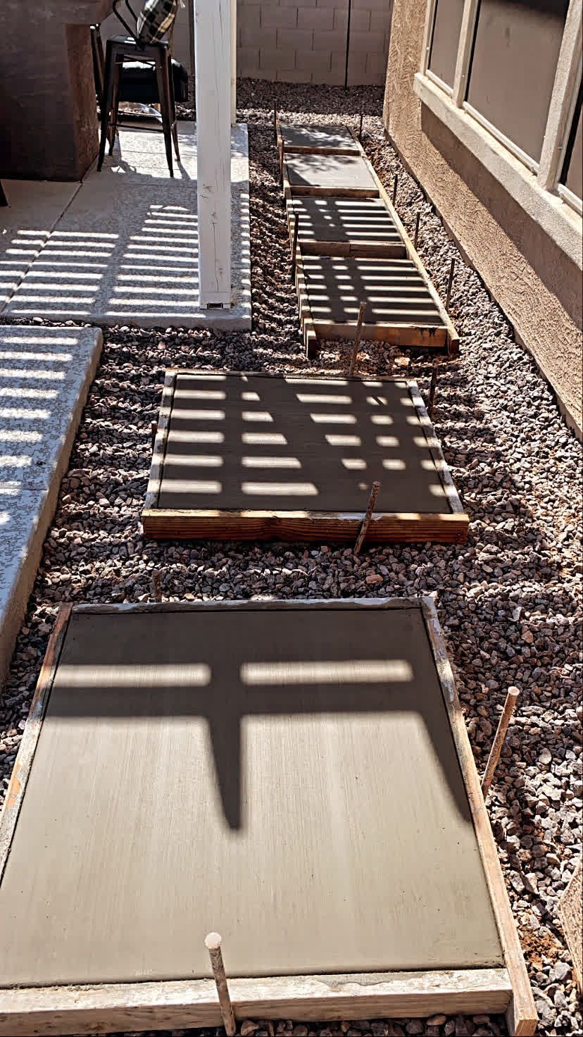 A concrete walkway is being built in the backyard of a house.