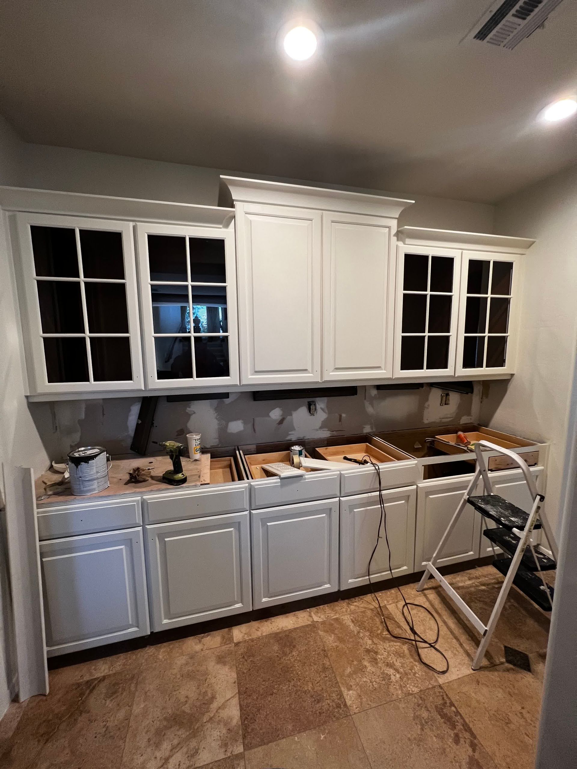 A kitchen under construction with white cabinets and a ladder