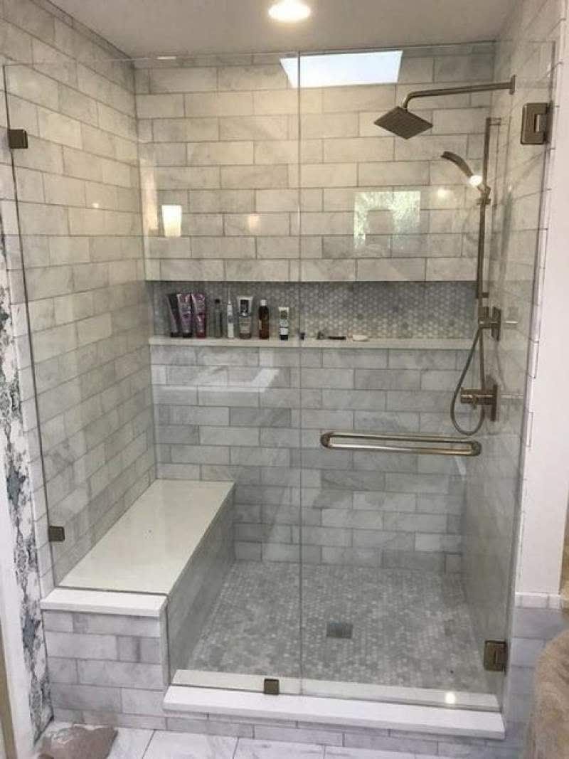 A bathroom with a walk in shower with a glass door and a bench.