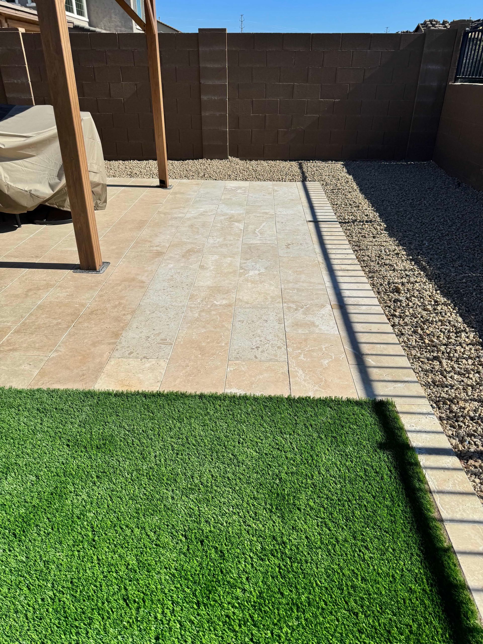 A patio with a brick wall and a brick walkway surrounded by grass and gravel.
